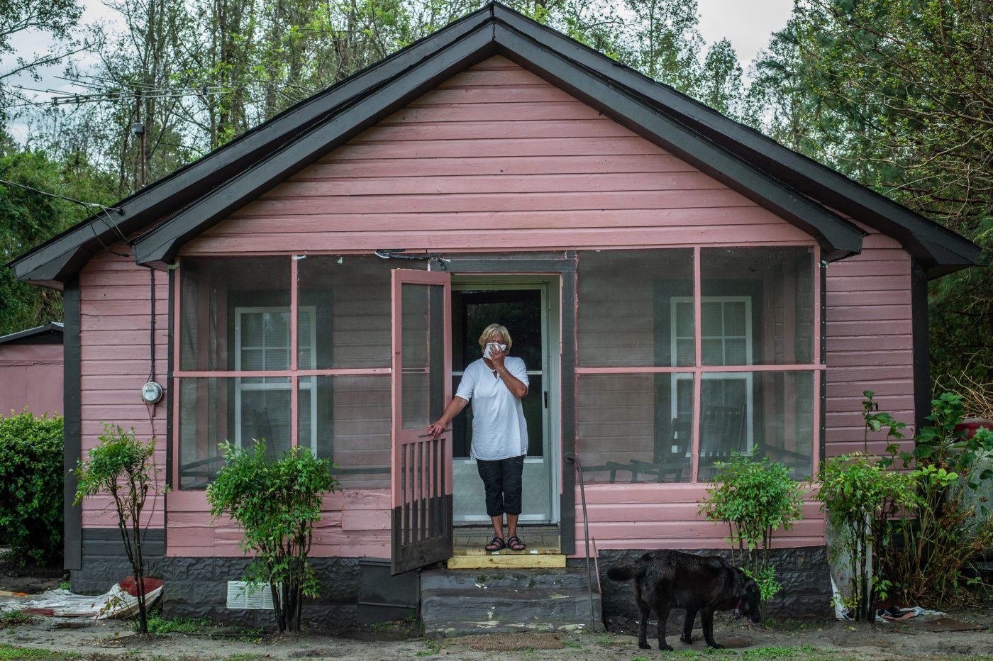 Vertical explainer photo 3 - Activist Elsie Herring, stands on the porch of her family home, holding a handkerchief over her mouth to filter out manure being sprayed on the field next door / Photo Credit: Jo-Anne McArthur / We Animals